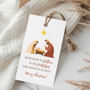 May include: A white gift tag with a Christmas nativity scene illustration. The tag features a star, and the text "Remember to follow in his footsteps this holiday season Merry Christmas!" is printed in brown.