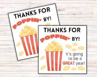 May include: Two square white gift tags featuring a watercolor illustration of a red and white striped popcorn bucket filled with yellow popcorn. The text reads THANKS FOR POPPIN' BY! and one tag includes the additional text It's going to be a GREAT year!
