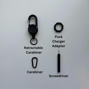 May include: A black retractable carabiner, a small black carabiner, a black octagonal puck charger adapter, and a thin black screwdriver. The items are labeled with the text Retractable Carabiner, Carabiner, Puck Charger Adapter, and Screwdriver.