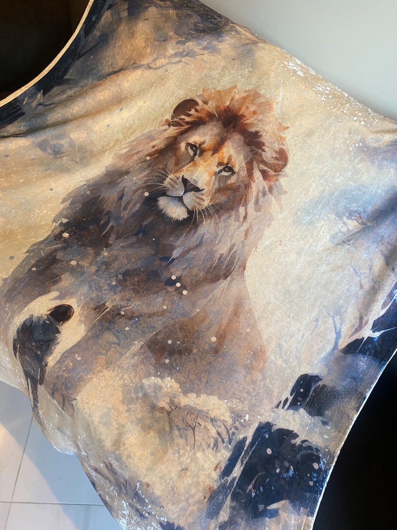 Op de afbeelding: Een aquarel schilderij van een leeuw op een beige achtergrond met blauwe en zwarte accenten. De leeuw kijkt naar voren met zijn mond dicht en zijn ogen open. Het schilderij heeft een zachte, dromerige uitstraling.