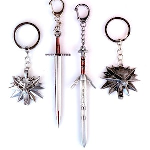 May include: Four metal keychains featuring two silver wolf head medallions and two sword pendants. The swords have red accents on the hilts and engraved markings on the blades. Each piece is attached to a silver-toned split ring by a short chain.