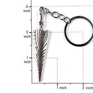 May include: A silver-toned metal keychain featuring a dagger-shaped pendant with an intricate engraved pattern of curved lines. The pendant measures approximately 2.5 inches in length, as indicated by the visible ruler markings in the image.