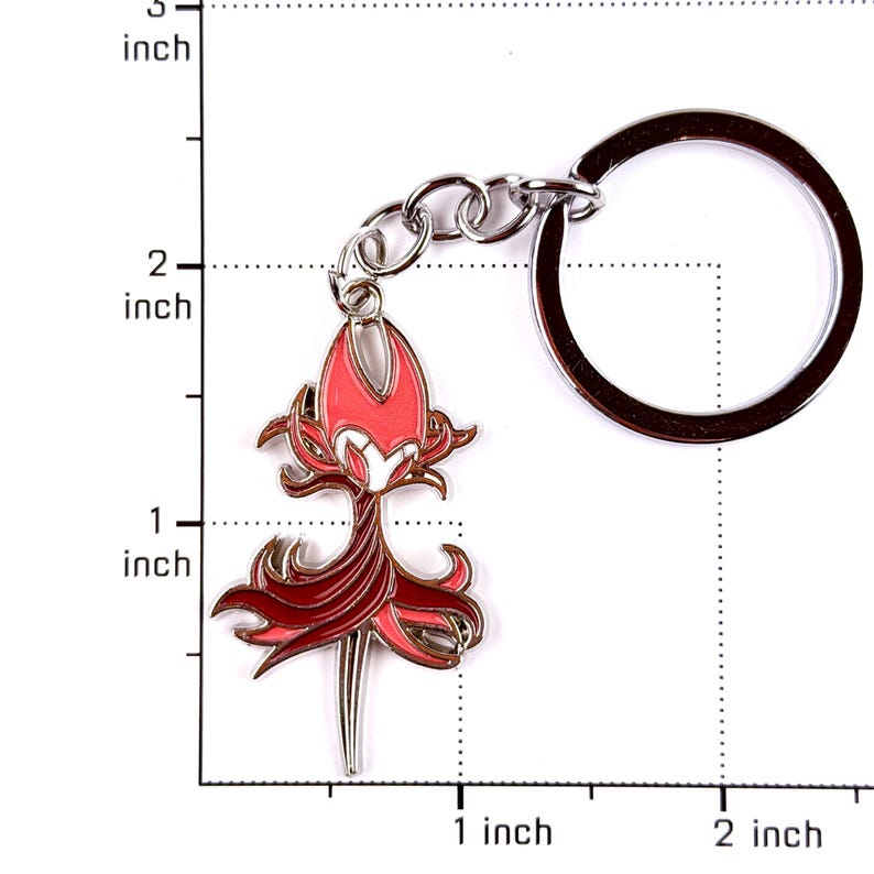 May include: A metal keychain featuring a character charm with a red and dark red color scheme, depicted with a pointed head and flowing lower section. The charm is attached to a silver-toned circular ring, with a visible scale showing a height of 1.5 inches.