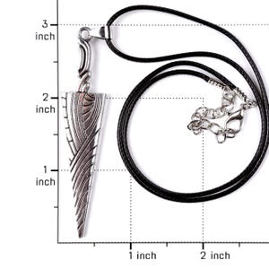 May include: A silver-toned metal pendant shaped like a stylized dagger with intricate engraved lines, suspended from a black cord necklace. A ruler overlay indicates the pendant length is approximately 2.5 inches and the width is 0.75 inches.