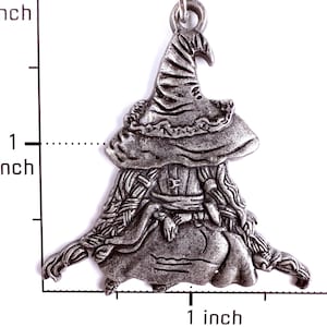 May include: A silver-toned metal charm shaped like a figure wearing a wide-brimmed pointed hat and a long garment. The charm is positioned against a white background with a ruler showing a height and width of approximately 1.5 inches.