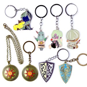 May include: Collection of metal keychains and a necklace. Keychains feature various character designs in vibrant colors, including a knight, a shield, and a character with green hair. The necklace has a circular pendant with a sun design.