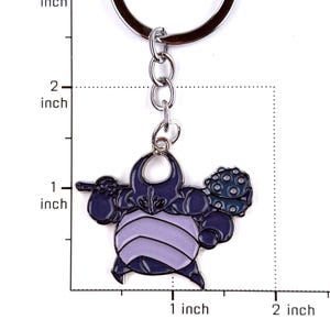 May include: A metal keychain featuring a dark purple and light lavender character charm with a spiked club. The charm is attached to a silver-colored split ring. A ruler graphic indicates the charm is approximately 1 inch wide and 1 inch tall.