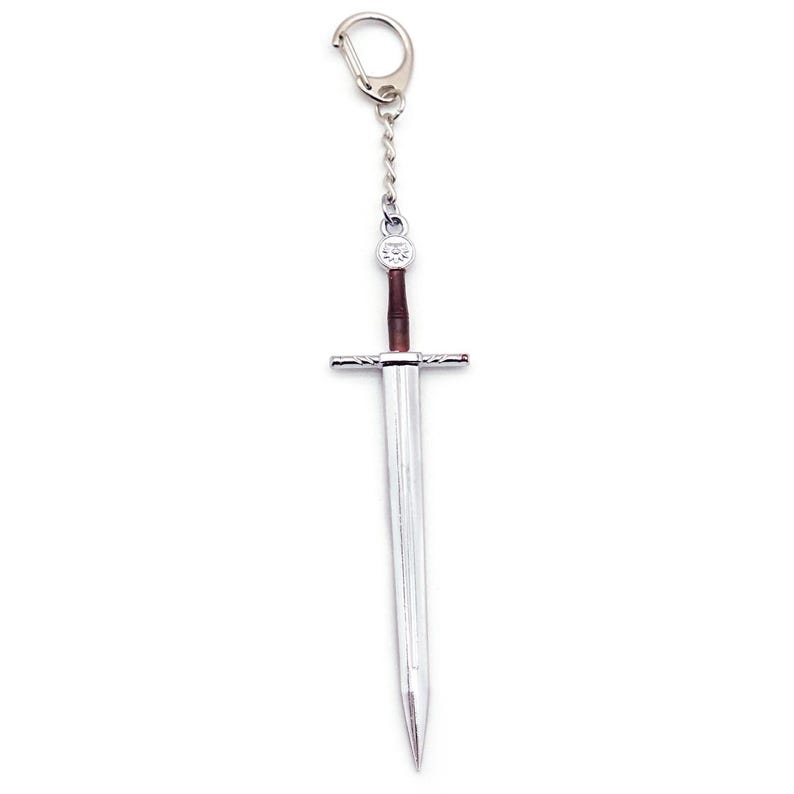 May include: A silver-toned metal sword keychain featuring a long, pointed blade, a straight crossguard, and a brown cylindrical handle. The sword is attached to a short silver chain and a circular metal split ring for secure attachment to keys.