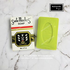 Op de afbeelding: Een doosje Siete Machos zeep en een groene zeep. De doos is wit met rode en gouden details, en bevat de tekst "Siete Machos SOAP" en een geitenillustratie. De zeep is heldergroen en weegt 90 gram.