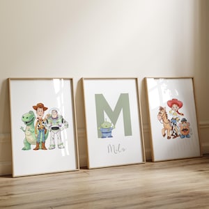 May include: Three framed prints featuring Toy Story characters. The prints include images of Rex, Woody, Buzz Lightyear, an alien, and Jessie. One print has the letter "M" and the name "Milo". The frames are light brown.