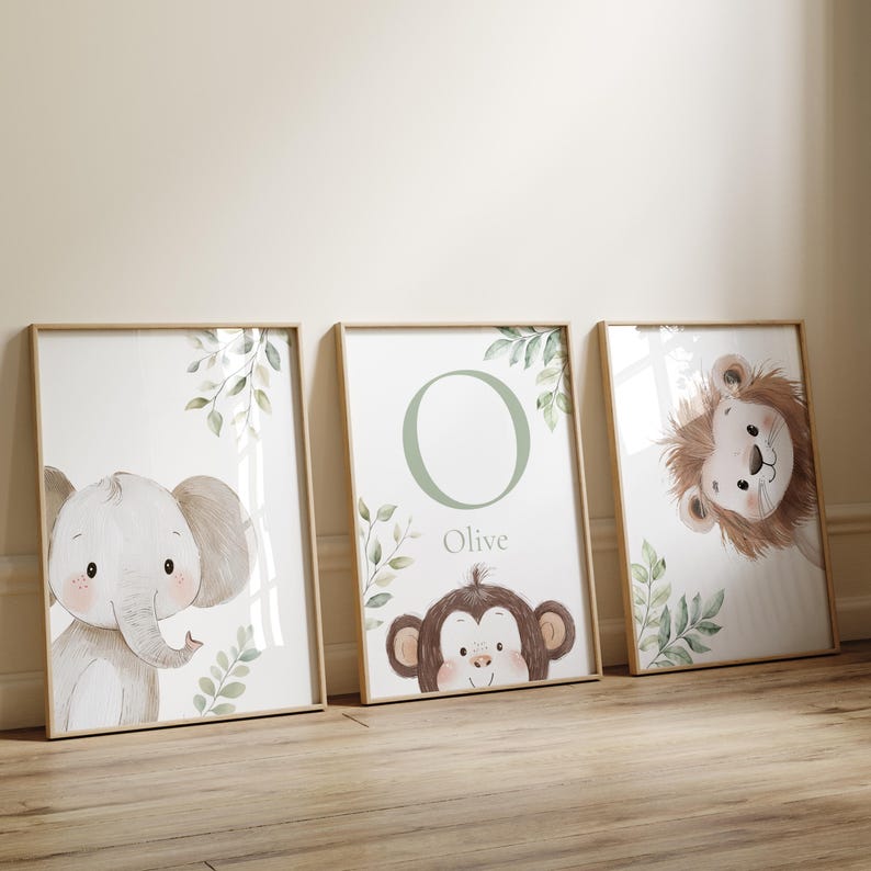 May include: Three framed nursery art prints featuring watercolor illustrations of animals. The prints include an elephant, a monkey with the name "Olive", and a lion. Each print has a light wood frame and botanical accents.