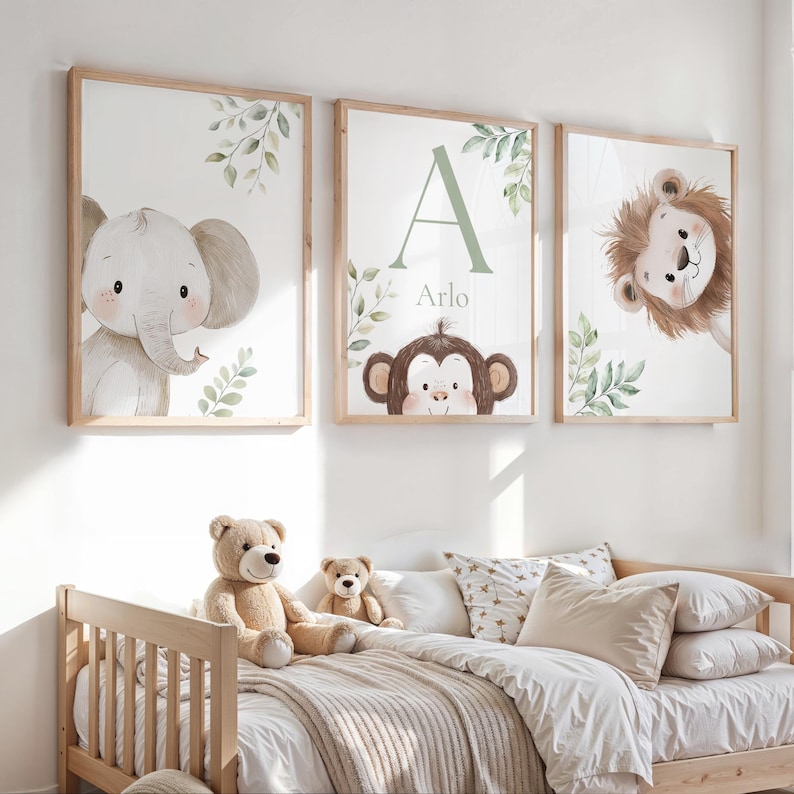 May include: Three framed animal art prints. The prints feature an elephant, a monkey with the name "Arlo", and a lion. Each print has a light wood frame and a watercolor style. Green leaves and foliage are also included in the design. The prints are displayed above a bed.