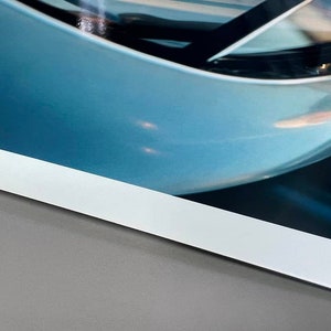 May include: Close-up of a blue and white photograph with a white border. The photograph shows a curved, blue surface with a reflection of light.