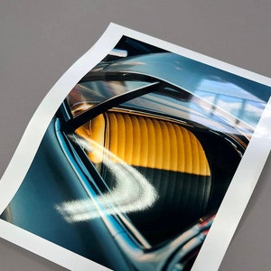 May include: A close-up of the interior of a classic car. The car has a yellow leather seat and a black dashboard. The car's window is rolled down, revealing the blue sky outside.