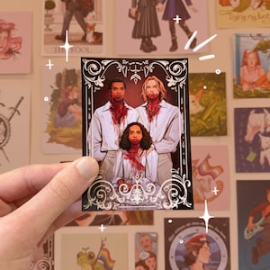 May include: A rectangular art print with three figures, their white shirts stained with a blood-like substance. The print is framed with black and white decorative flourishes. Other art prints are visible in the background.