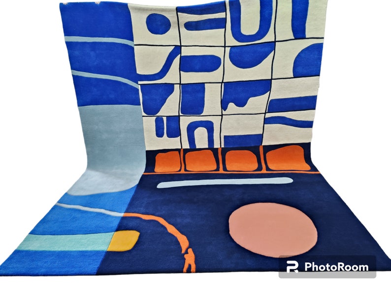 May include: An abstract rug with a modern design in blue, orange, and cream. The rug has a dark blue base with a lighter blue and cream-coloured pattern. An orange border and a peach-coloured circle add to the design.