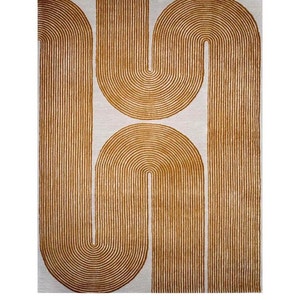 Puede incluir: Una alfombra rectangular con un fondo color crema y un patrón repetitivo de líneas curvas de color marrón dorado. Las líneas crean una serie de formas de U y semicírculos conectados, dando a la alfombra un diseño geométrico moderno. La alfombra probablemente está hecha de un material suave y tejido.