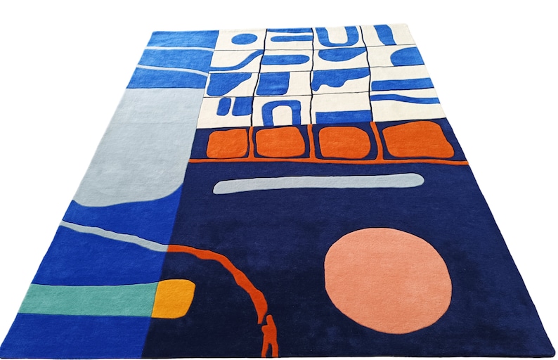 May include: Modern geometric rug in navy blue, light blue, orange, and white. The rug has an abstract design with a large peach circle and other shapes. The rug is rectangular in shape and would suit a living room.
