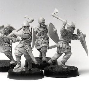 Könnte beinhalten: Eine Gruppe unbemalter Miniaturfiguren, die mittelalterliche Krieger in Aktion darstellen. Jede Figur ist mit detaillierter Rüstung bekleidet und schwingt Äxte und Schilde. Die Miniaturen stehen auf schwarzen Sockeln, bereit zum Bemalen und Ausstellen.