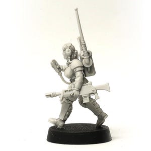 May include: A grey miniature figure of a female soldier in a running pose. She is equipped with a rifle, backpack, headset, and a handheld device. The figure is mounted on a black base, showcasing a detailed design.