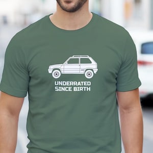 Può includere: T-shirt verde con grafica bianca di un'auto e la scritta "UNDERRATED SINCE BIRTH". La grafica dell'auto è un profilo laterale di un piccolo veicolo squadrato. La maglietta è di colore verde unito.