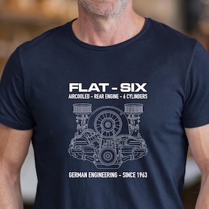 Puede incluir: Una camiseta azul marino con un gráfico de líneas blancas de un motor bóxer de seis cilindros refrigerado por aire. El texto dice: FLAT-SIX, AIRCOOLED - REAR ENGINE - 6 CYLINDERS y GERMAN ENGINEERING - SINCE 1963. El diseño está centrado en el pecho.
