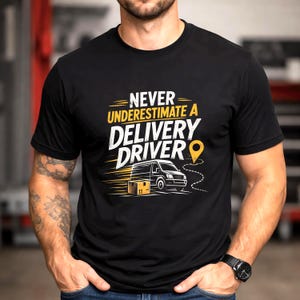 May include: A black short-sleeved t-shirt featuring a graphic print with the text NEVER UNDERESTIMATE A DELIVERY DRIVER in white and yellow. The design includes a white delivery van, a brown cardboard box, and a yellow location pin icon.