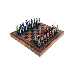 May include: A chess set with intricately designed pieces in blue, red, and white. The chess board is square, with a brown and black checkered pattern, and a decorative border. The pieces are arranged for play.