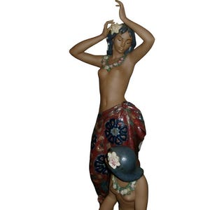 Può includere: Statua in ceramica di due figure, una in piedi e una in ginocchio. La figura in piedi ha le braccia alzate, indossa un involucro rosso e blu a fantasia e una ghirlanda di fiori. La figura in ginocchio indossa un cappello blu e una ghirlanda di fiori.