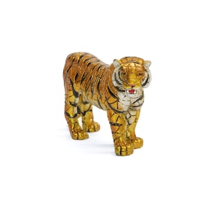 May include: A detailed figurine of a tiger, standing on all fours. The tiger has a gold and brown color scheme with black stripes. The tiger's mouth is open, revealing a red interior. The figurine is set against a white background.