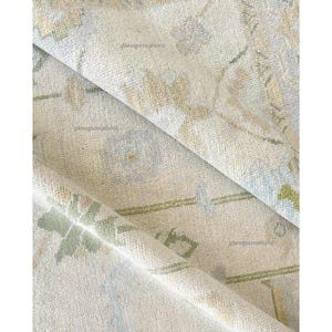 May include: Close-up of a rolled-up area rug with a faded floral pattern in shades of cream, green, and blue. The rug has a soft, textured appearance, with the text "phrugcreations" visible in several places.