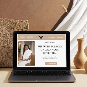 Op de afbeelding: Een laptopcomputer waarop een website voor een lifecoach wordt weergegeven. De website toont een foto van een vrouw en de tekst "Rise with Purpose: Unlock Your Potential. Ignite Your Power, Embrace Your Strength, Transform Your Life. Learn More."