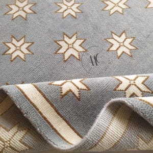 May include: A light blue rug with a repeating pattern of white and brown starbursts. The rug's border features stripes of white and brown. The rug is folded over, revealing the underside and the edge of the design.