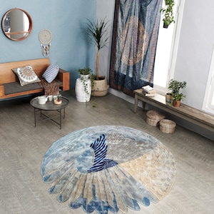 May include: A round blue, gray, and beige rug with a stylized peacock design. The rug is in a living room with a couch, a coffee table, and plants.