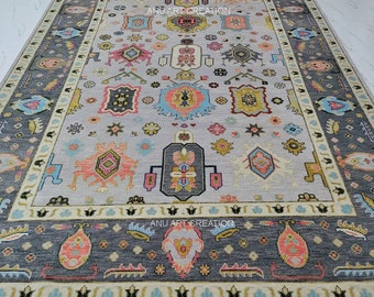May include: A gray rug with a colorful geometric pattern. The rug has a light gray background with a darker gray border. The pattern includes various shapes and colors, including pink, blue, yellow, and green. The rug is made of wool and has a fringe border.