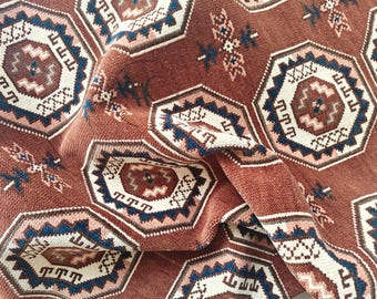 Puede incluir: Primer plano de un textil tejido con un patrón geométrico repetitivo. El diseño presenta formas octogonales en tonos marrón, crema y azul. La tela tiene una apariencia texturizada, con hilos visibles y una caída suave.