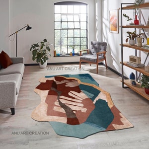 May include: Abstract area rug with a modern design featuring shades of brown, beige, blue, and teal. The rug has an irregular shape and is shown in a living room setting.