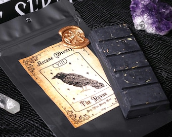 May include: A black bag with a gold wax seal and a tarot card design featuring a raven with the text "Arcane Wiccery VIII The Raven Soy Wax Snap Bar 100g".