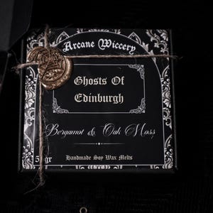 May include: A black box with a gold wax seal and white text that reads "Arcane Wiccery", "Ghosts of Edinburgh", "Bergamot & Oak Moss", and "Handmade Soy Wax Melts".