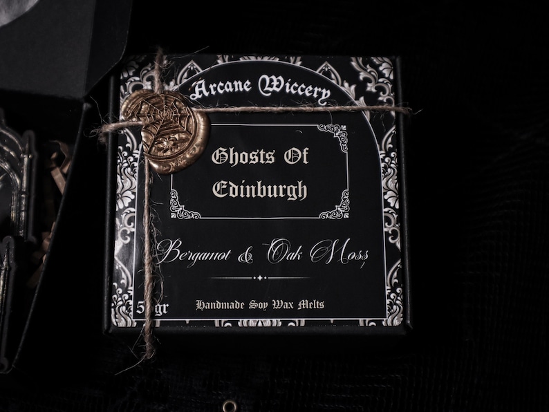 May include: A black box with a gold wax seal and white text that reads "Arcane Wiccery", "Ghosts of Edinburgh", "Bergamot & Oak Moss", and "Handmade Soy Wax Melts".