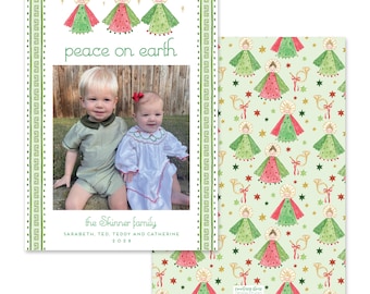 Puede incluir: Una tarjeta de Navidad con una foto de dos niños y el texto "peace on earth". El diseño de la tarjeta incluye ilustraciones de ángeles con vestidos rojos y verdes. El reverso de la tarjeta tiene un patrón repetido de ángeles, estrellas y trompetas.
