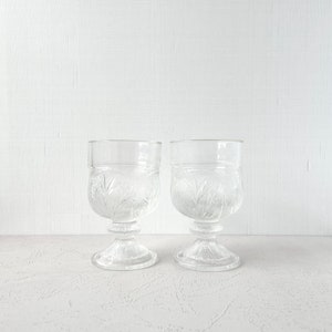 Könnte beinhalten: Zwei klare Glaskelche mit einem geschliffenen Glasdesign. Die Kelche haben eine runde Schale und einen Stiel mit einer runden Basis.