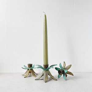 Puede incluir: Tres candelabros de palma de oro con hojas verdes. El candelabro del centro tiene una vela verde.