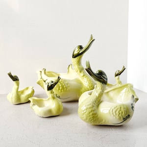 Puede incluir: Conjunto de cuatro macetas de cerámica en forma de cisne de diferentes tamaños. Las macetas son de color amarillo pálido con detalles verdes y presentan un diseño de cisne detallado.