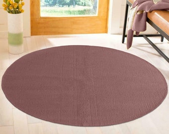 May include: A round, mauve-colored rug with a textured surface. The rug is placed on a light wood floor.