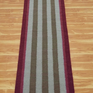 May include: A long, narrow runner rug with a striped pattern. The rug has a burgundy border and features alternating stripes of light gray and brown.