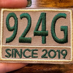 May include: Embroidered patch with the text "924G" in dark green, above "SINCE 2019" in a rectangular tan shape with a gold border. The patch is rectangular and has a tan background.
