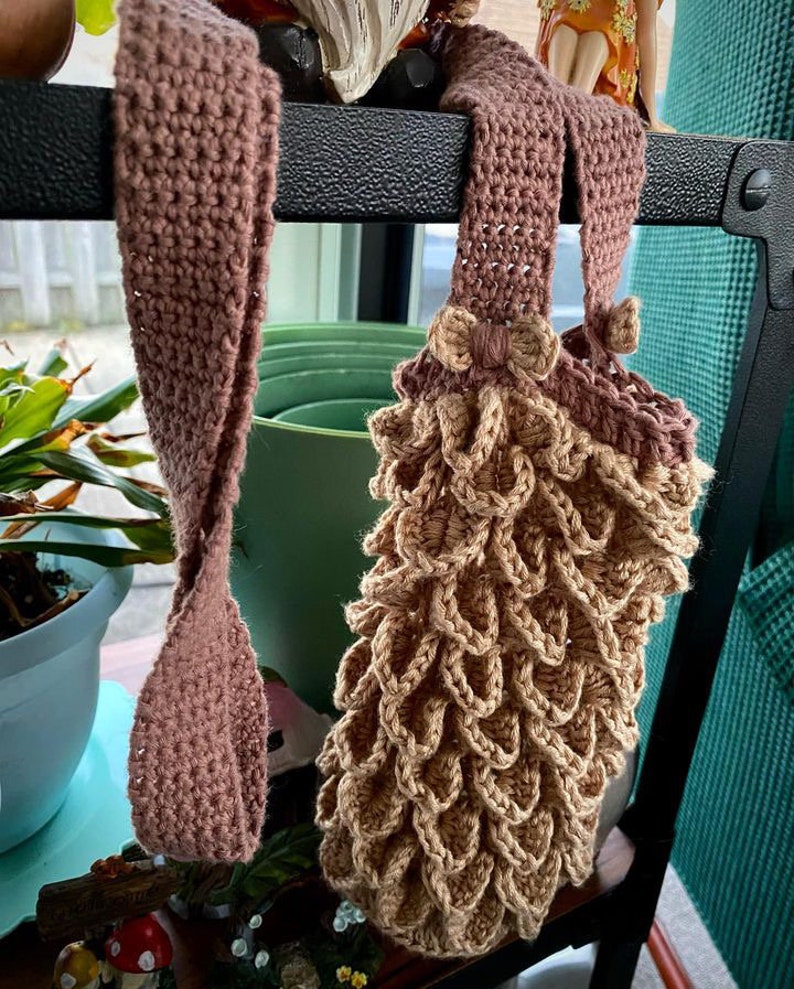 May include: Two crocheted bags hanging on a shelf. One bag is brown and the other is a light brown with a textured, scale-like pattern.