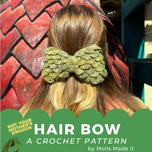 May include: Green crochet hair bow with a scale pattern. The bow is tied in a knot and is worn by a person with long brown hair. The text on the image reads "Not Your Mother's Dragon" and "Hair Bow A Crochet Pattern by Molls Made It".