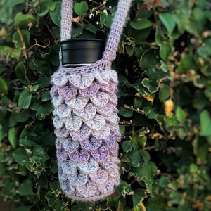 May include: A purple and white crocheted bottle holder with a strap. The holder is made with a scale pattern and is designed to fit a standard-sized water bottle.